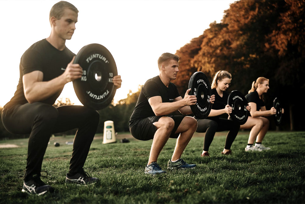 2 men and 2 women doing a squat iwth a a weight